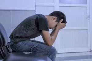 A man sitting on a chair with his head in his hands. A child feels lonely and holds his head in pain.