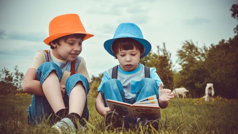 Two kids reading a book outside.